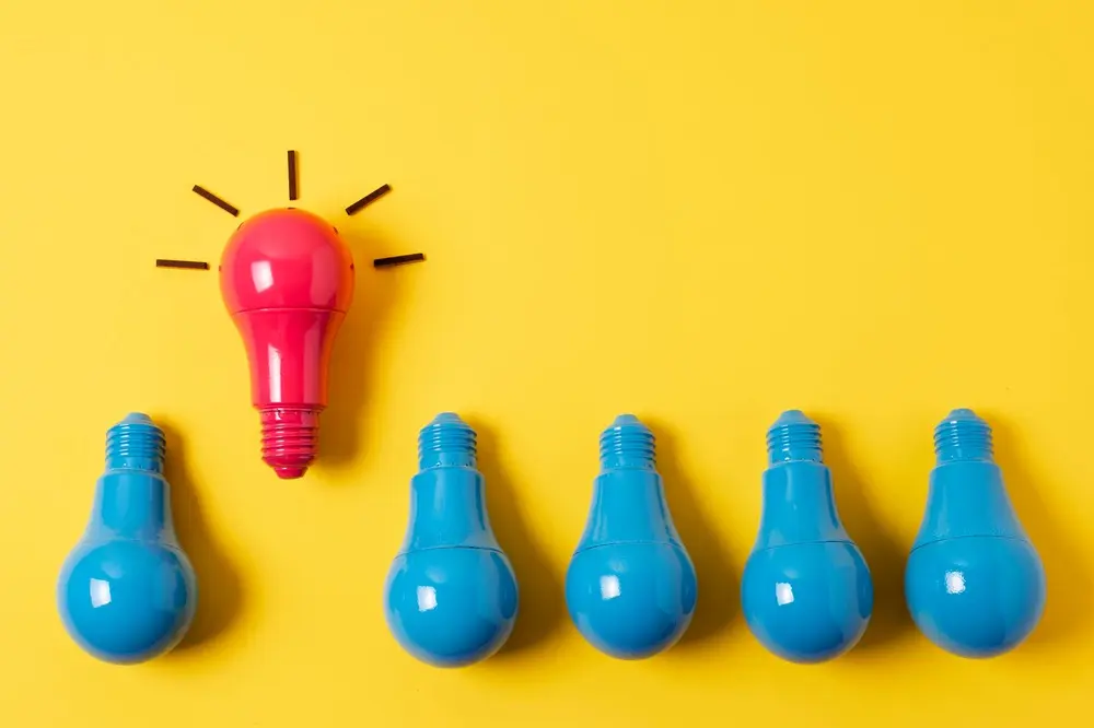 Five blue lightbulbs and one standout red lightbulb on a yellow background