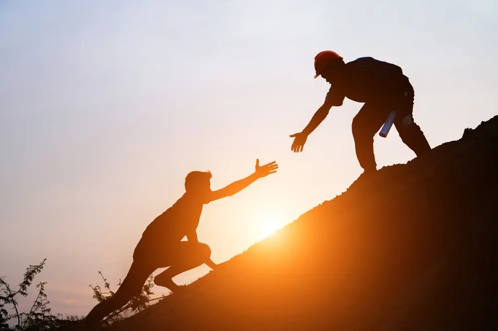 On a mountain, one climber extends a hand to help another climber ascend